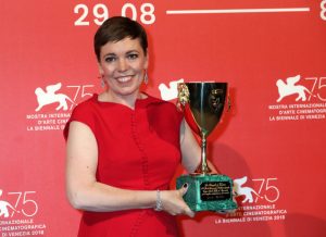 Picture shows Olivia Colman with short hair, stood in front of a red background holding her best actress trophy